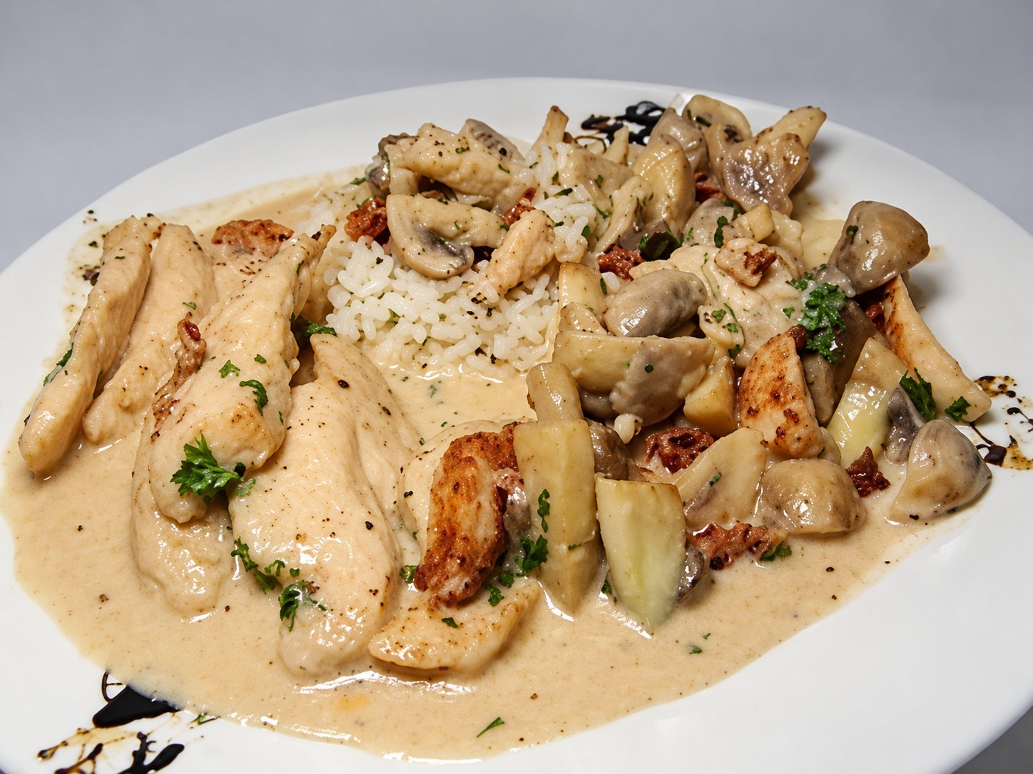 Une assiette blanche garnie d’émincés de poulet dans une sauce crémeuse, accompagnés de champignons, de lardons et de riz.