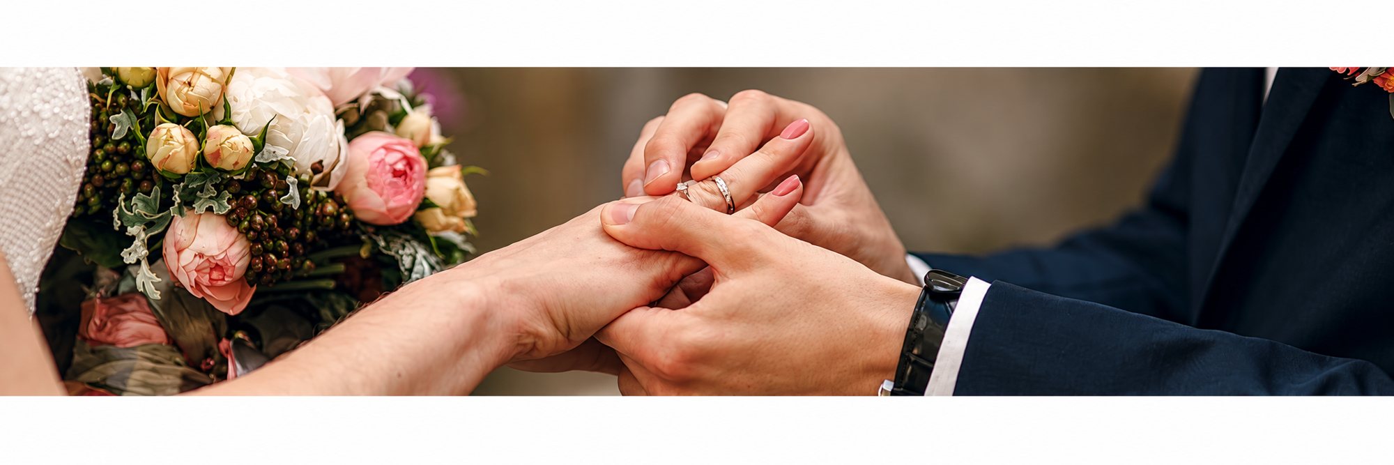 Une mariée glisse une alliance au doigt du marié, à côté d’un bouquet de roses pêche.