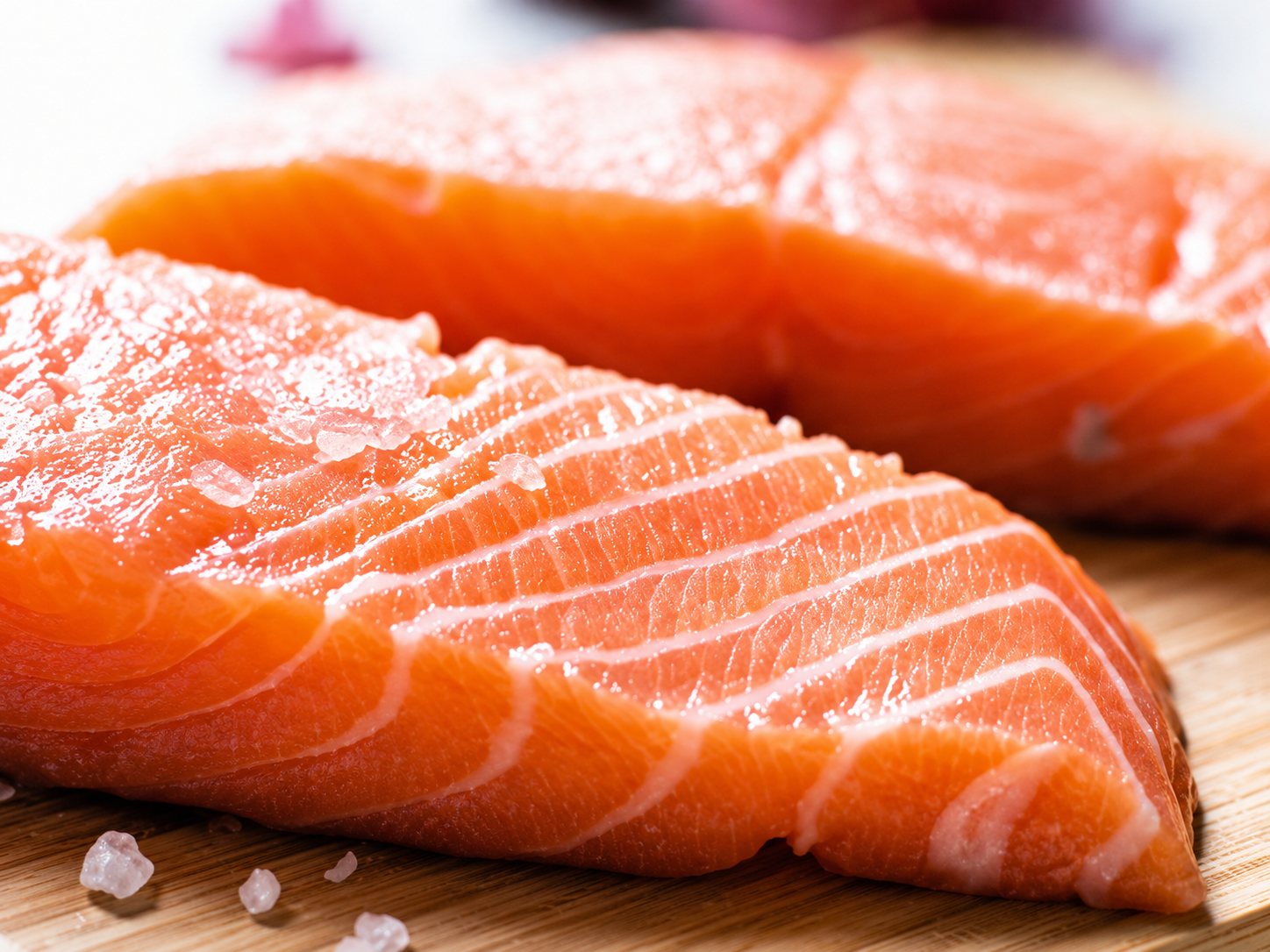 Gros plan sur deux filets de saumon cru posés sur une planche en bois, saupoudrés de cristaux de sel.