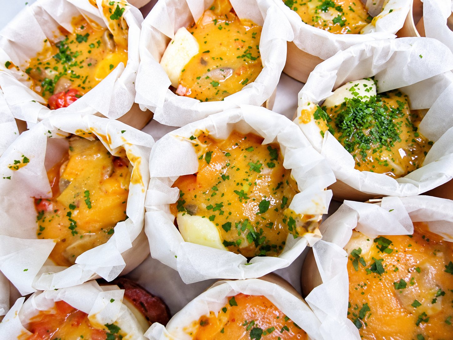 Vue de dessus de plusieurs petits gratins dorés parsemés de persil, servis dans des caissettes en papier blanc.
