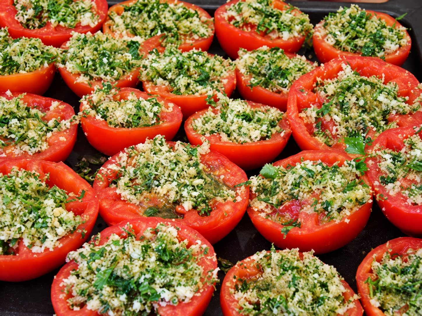 Des moitiés de tomates garnies d’une persillade et de chapelure sont disposées côte à côte sur une plaque de cuisson.