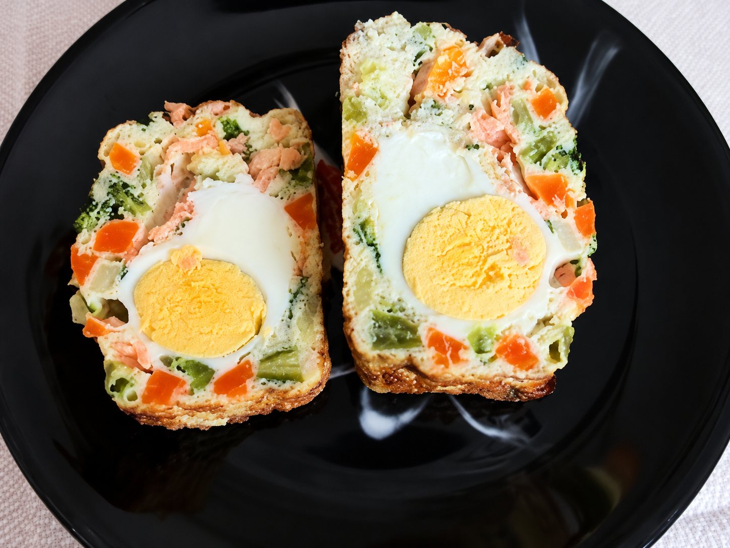 Deux tranches de terrine colorée aux carottes, haricots verts et saumon, avec un demi-œuf dur au centre, posées sur une assiette noire.